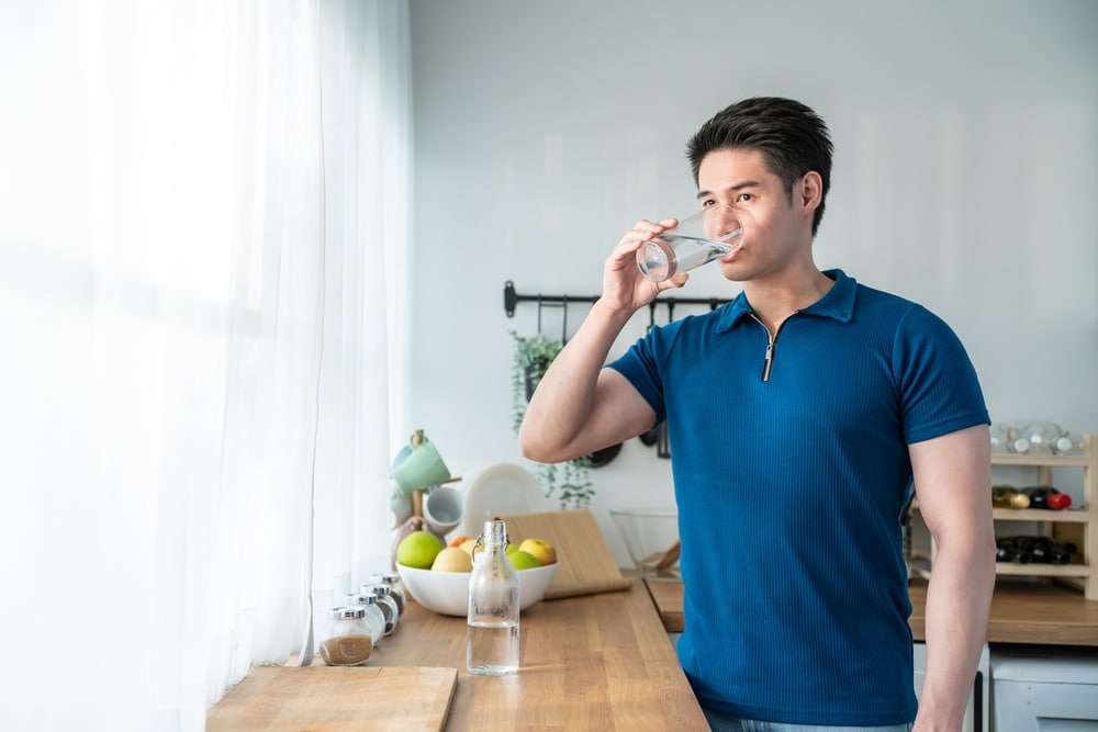 Man in his kitchen drinking water for his overall health and wellness.