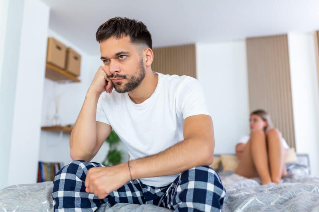 Upset young man sitting on edge of bed and experiencing symptoms of low testosterone