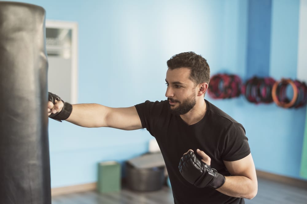 Man in a gym practices boxing by jabbing a punching bag